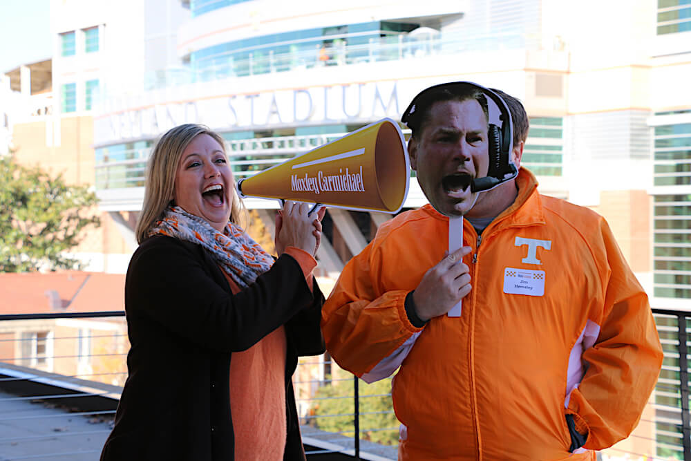 Everyone loves props! Danielle Hemsley of Johnson Architecture with her husband, Jim, behind the Butch Jones picture, at the Moxley Carmichael tailgate.